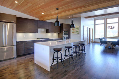 New construction Banff Canmore white kitchen room open concept hardwood floors wood contemporary industrial wood stairs metal railings stainless steel appliances steel fireplace wood roof feature white wood wall 