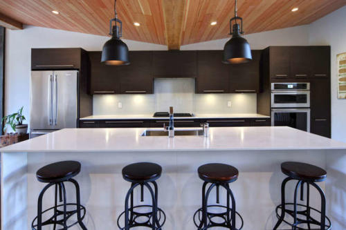 New construction Banff Canmore white kitchen room open concept hardwood floors wood contemporary industrial wood stairs metal railings stainless steel appliances steel fireplace wood roof feature white wood wall 